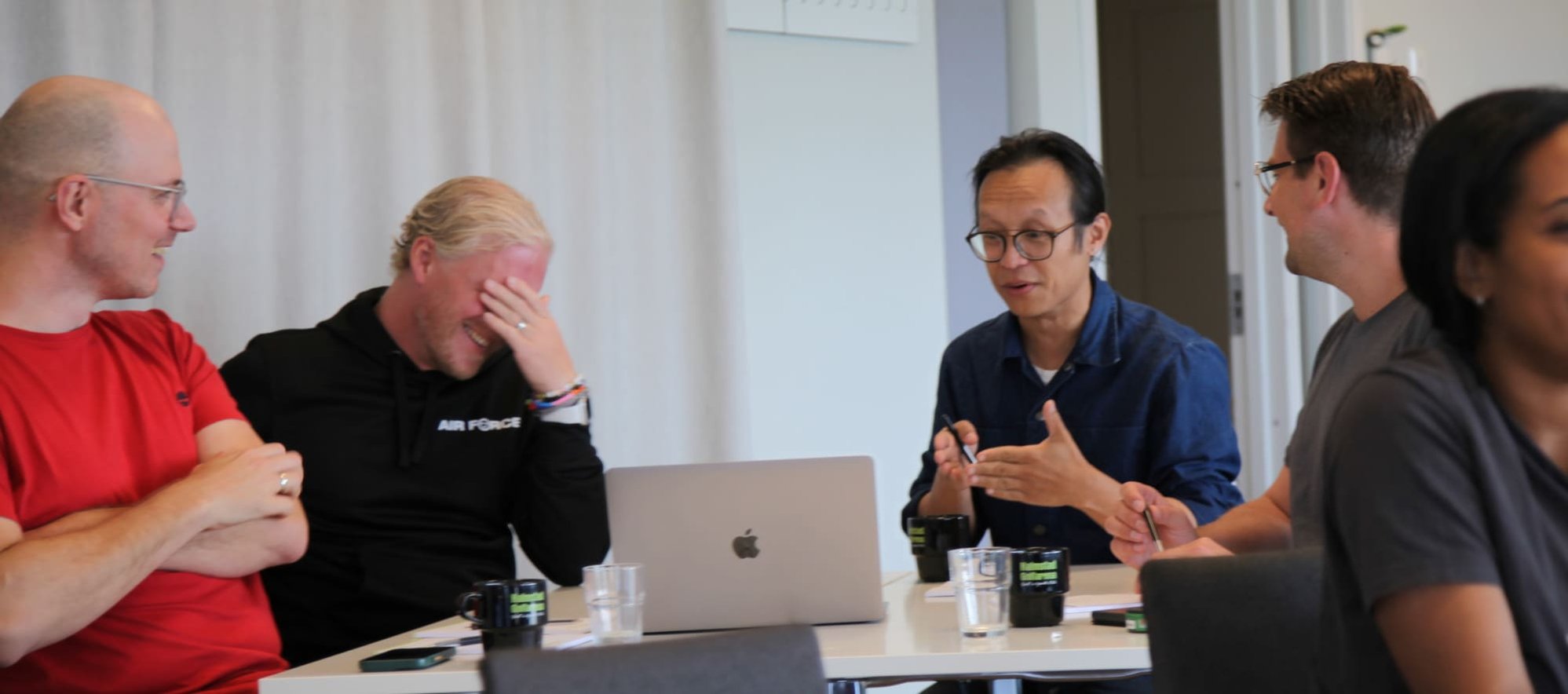 A group of colleagues gathered around a table in a workshop setting, laughing and enjoying a collaborative moment together.