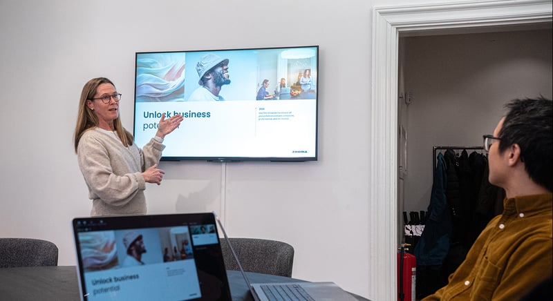 A woman presenting slides on a screen during a meeting while colleagues watches