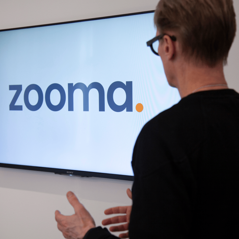 Man in front of a screen showing the Zooma logo