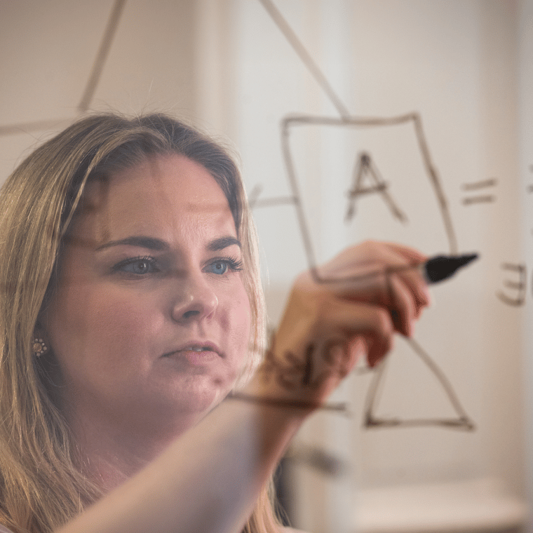 Woman writing a diagram on glass, focusing on a box labeled “A.”