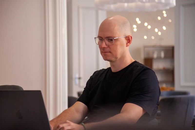 Person med glasögon som arbetar på en bärbar dator vid ett bord i en ljus, modern kontorsmiljö, fokuserad på skärmen