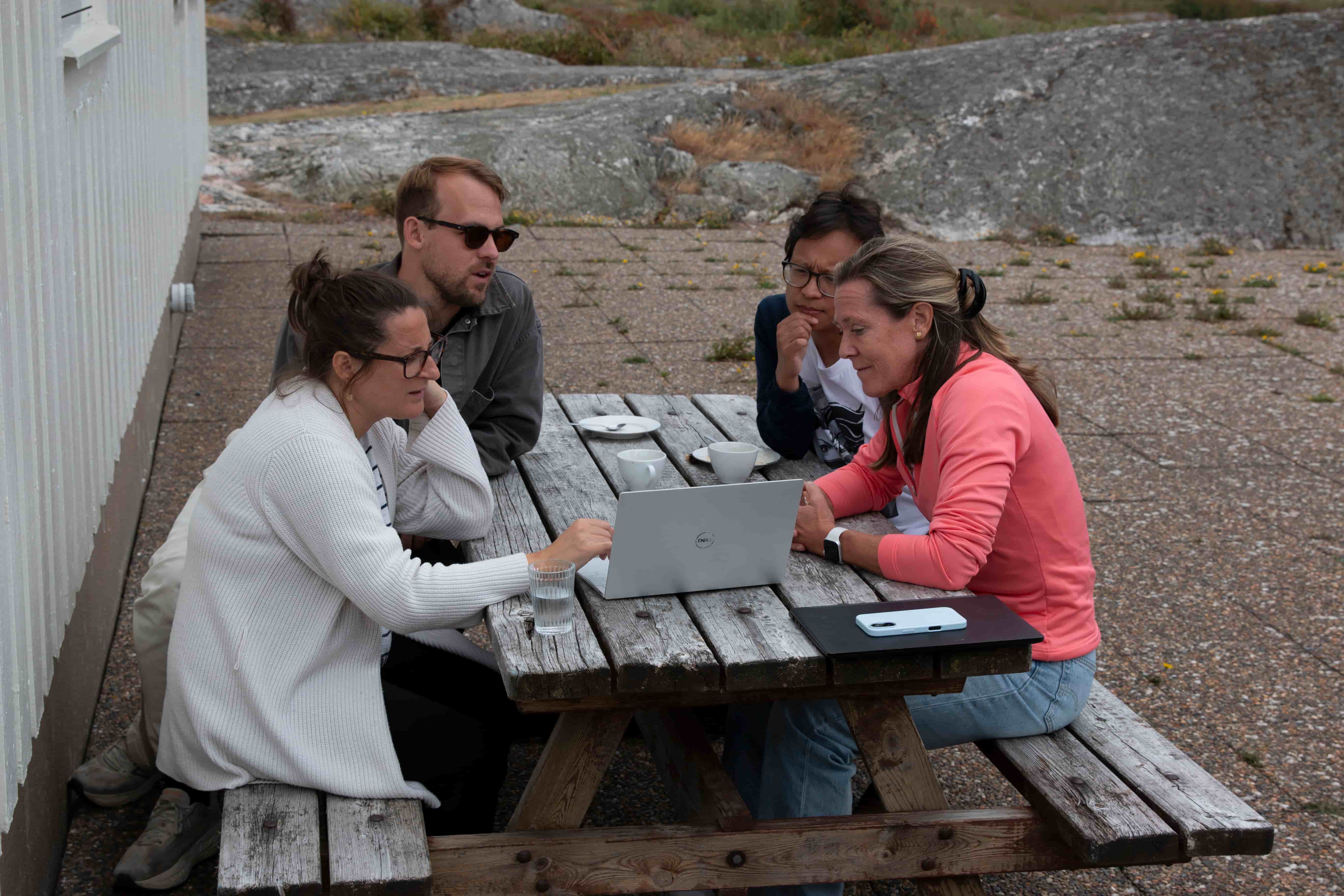 Small group of colleagues collaborating outdoors at a wooden table with a laptop during the Zooma kick-off on Vrångö