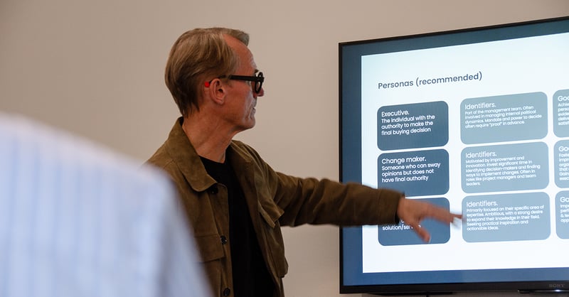 A man points to a presentation slide about recommended personas during a meeting.